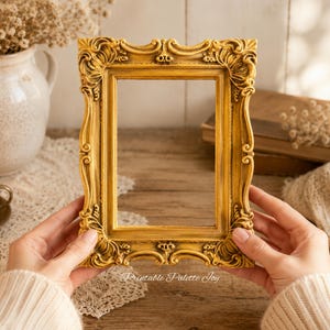 May include: A rectangular picture frame with an ornate, raised gold-toned border featuring intricate scrollwork and decorative carvings. The frame has a weathered finish with darker highlights in the recessed areas, creating a textured appearance.