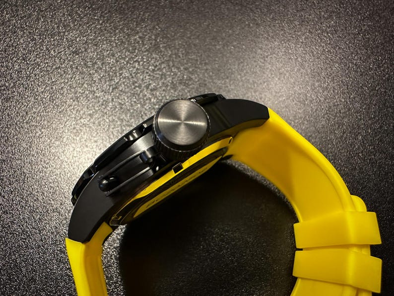 May include: A black wristwatch with a yellow strap. The watch features a black face and a silver crown. The yellow strap is made of a flexible material.