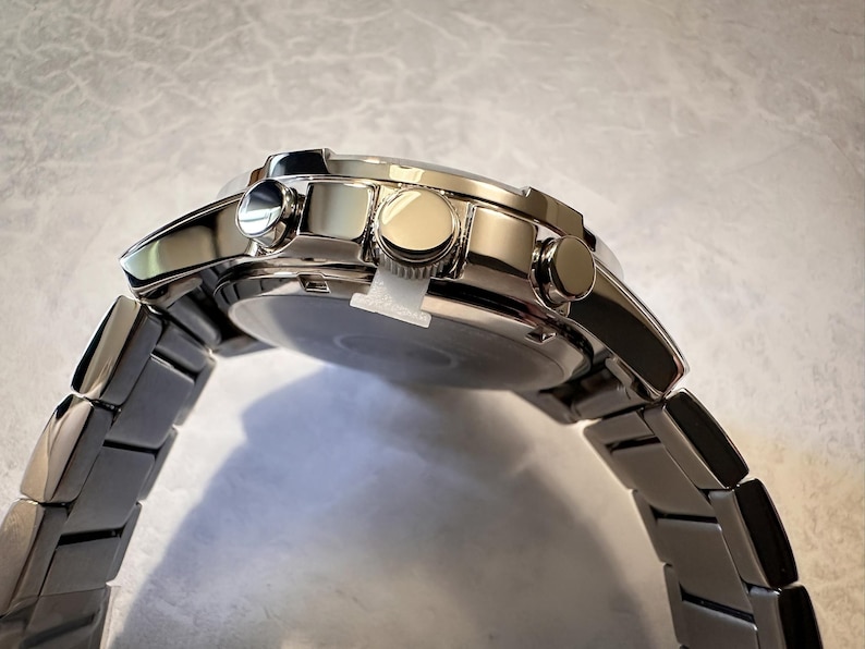 May include: A stainless steel wristwatch with a silver band and a round face. The watch has three buttons on the side and a polished finish. The watch band is made of rectangular links.