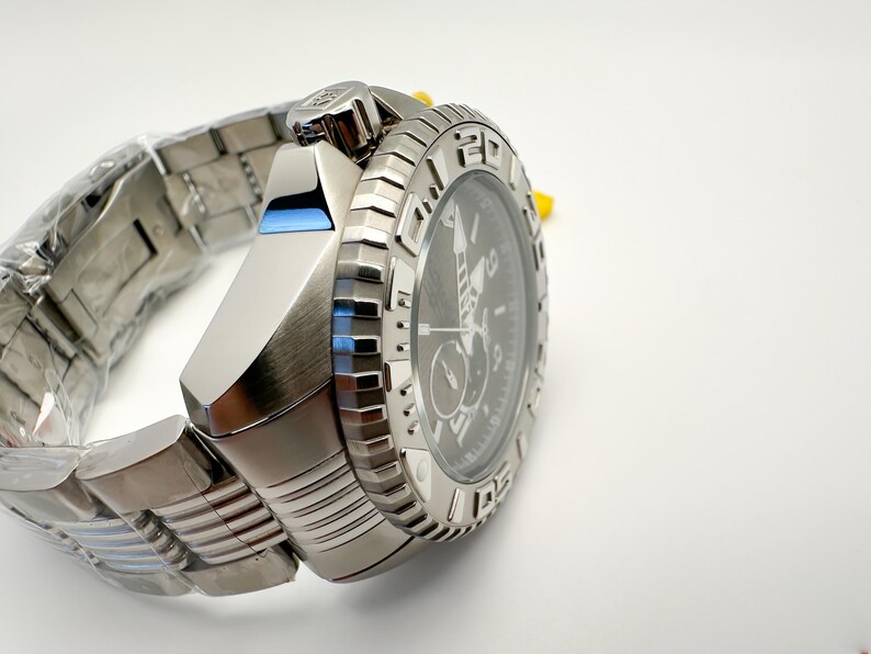 May include: A silver wristwatch with a black dial and a textured bezel. The watch has a stainless steel strap and a blue accent on the side. The watch is new and still has protective plastic on the strap.