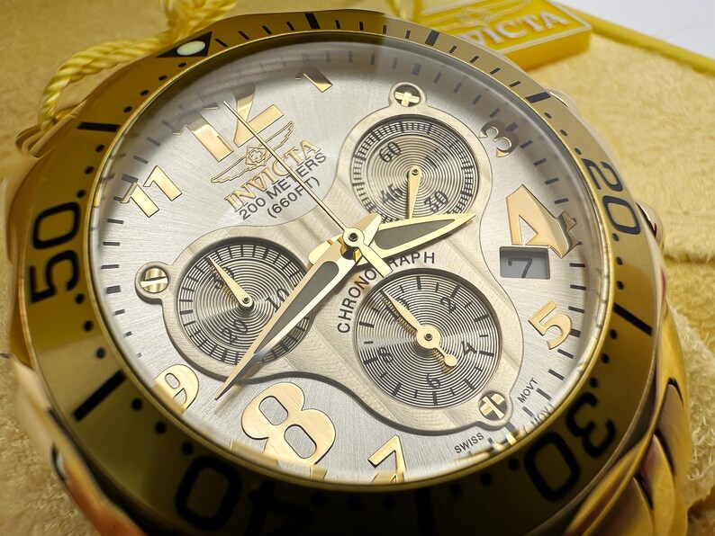 May include: Gold-toned Invicta chronograph watch with a silver dial. Features include three sub-dials, luminous hands, and a date window. The watch is water-resistant to 200 meters (660 feet).