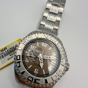 May include: A silver Invicta automatic watch with a brown face and a stainless steel strap. The watch has a visible mechanism and is marked with the numbers 6, 12, and 4. The watch is new and still has the original packaging.
