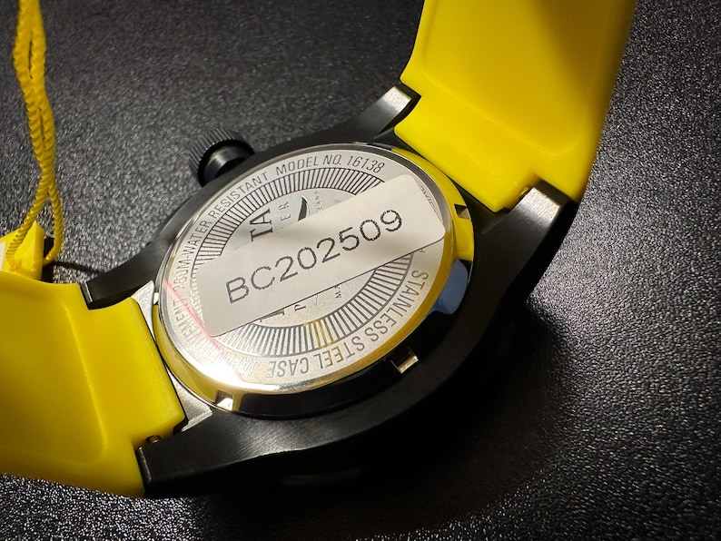 May include: A close-up shot of a black watch with a yellow strap. The watch features a stainless steel case and a black crown. The watch back has a sticker with the text "BC202509". The watch is water resistant to 300m.