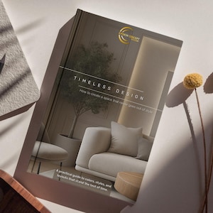 May include: A book titled "TIMELESS DESIGN" with a gold logo, featuring interior design elements. The cover displays a modern living room with a sofa, chair, and a tree in a pot. The book's subtitle reads, "How to create a space that never goes out of style."