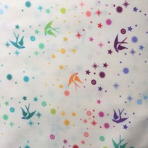 Puede incluir: Tela blanca con un patrón repetitivo de estrellas de colores, círculos y pájaros azules estilizados. El fondo es blanco con un efecto acuarela azul y verde sutil y descolorido.