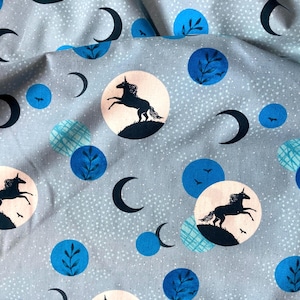 May include: Light blue fabric with a repeating pattern of black unicorns, crescent moons, and blue circles with leaf and bird designs. The fabric has a speckled background and is suitable for various craft projects.