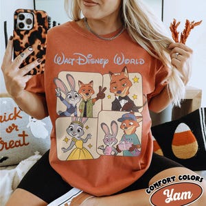 Peut inclure: T-shirt orange br&ucirc;l&eacute; avec des personnages du film Zootopie, avec le texte "Walt Disney World" en haut. Le motif comprend Judy Hopps, Nick Wilde et d'autres personnages dans une grille carr&eacute;e. Le t-shirt porte une &eacute;tiquette "Comfort Colors".