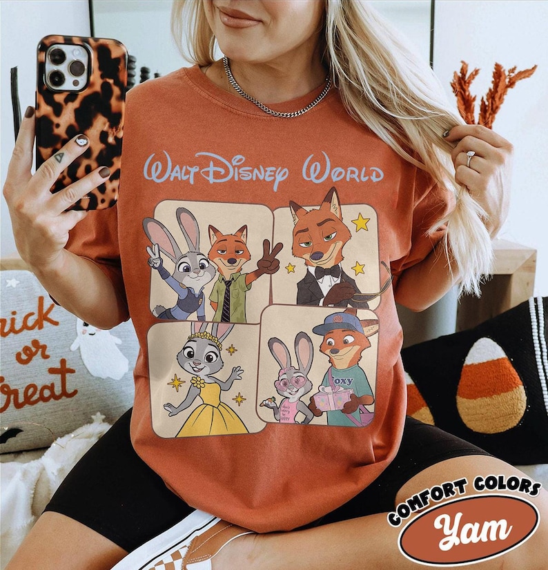Peut inclure: T-shirt orange br&ucirc;l&eacute; avec des personnages du film Zootopie, avec le texte "Walt Disney World" en haut. Le motif comprend Judy Hopps, Nick Wilde et d'autres personnages dans une grille carr&eacute;e. Le t-shirt porte une &eacute;tiquette "Comfort Colors".