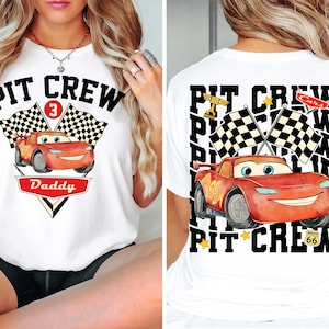 May include: White t-shirt featuring a cartoon image of a red race car with the text "PIT CREW" and "Daddy". The front design includes a number 3 and checkered flags. The back of the shirt also has a race car design and the text "PIT CREW".