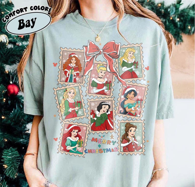 May include: A light green t-shirt featuring a design of various princesses in Christmas-themed postage stamps. A large red bow is at the top, with the words "Merry Christmas" below the stamps. The shirt has the words "Comfort Colors Bay" at the top.