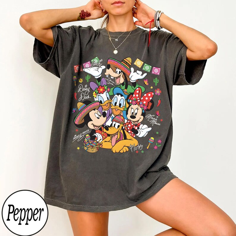 May include: Dark grey t-shirt with a vibrant graphic of Disney characters Mickey Mouse, Minnie Mouse, Donald Duck, Daisy Duck, Goofy, and Pluto in festive outfits. The shirt has the text "Mickey Mouse" and "Minnie Mouse".