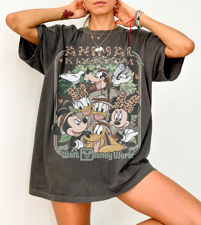 May include: Dark gray t-shirt featuring a graphic of Disney characters, including Mickey and Minnie Mouse, Donald and Daisy Duck, Goofy, and Pluto. The shirt has the text "Animal Kingdom" and "Walt Disney World" in a vintage style.