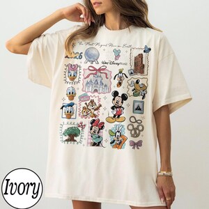 K&ouml;nnte beinhalten: Cremefarbenes T-Shirt mit einem Disney-Design, das Charaktere wie Mickey Mouse und Donald Duck sowie ikonische Bilder zeigt. Das Shirt enth&auml;lt den Text "The Most Magical Place on Earth" und "Walt Disney World".