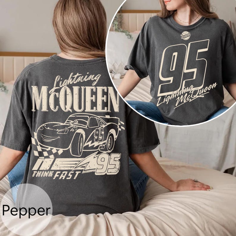 May include: Dark gray t-shirt featuring Lightning McQueen graphics. The front displays a large "95" with "Lightning McQueen" text. The back showcases a car illustration, the number "95", and the words "Lightning McQueen" and "Think Fast".