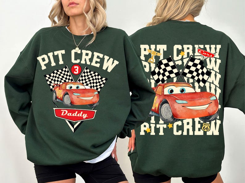 May include: Dark green sweatshirt with a graphic of Lightning McQueen from the movie Cars. The front features the text "PIT CREW" above a checkered flag and the number 3. Below is the word "Daddy" in a red and white design.