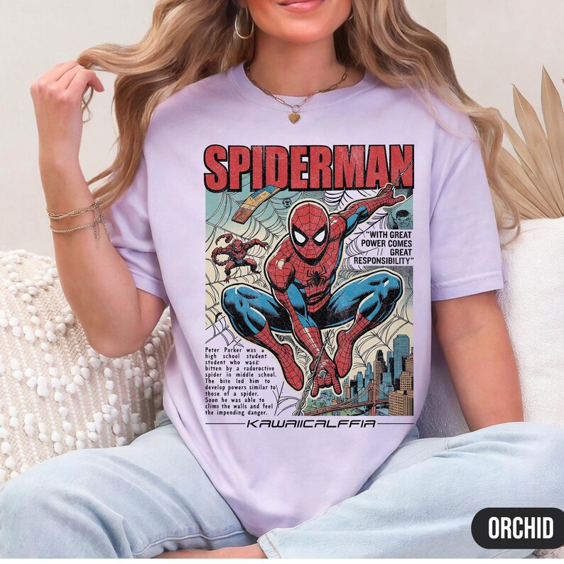 May include: Orchid-colored t-shirt featuring a vintage comic book-style illustration of Spiderman. The design includes the word "SPIDERMAN" in bold red letters, along with the quote "WITH GREAT POWER COMES GREAT RESPONSIBILITY". The shirt also has the text "KAWAIICALFFIA".