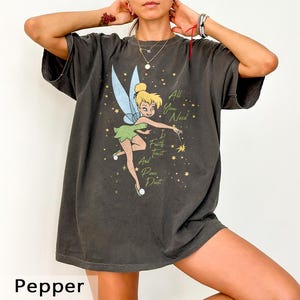 May include: Dark grey t-shirt featuring a graphic of Tinkerbell with light blue wings and a green dress. The text "All You Need Is Faith Trust And Pixie Dust" is printed on the shirt. The shirt is a relaxed fit.