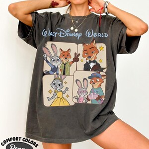 Peut inclure: T-shirt gris fonc&eacute; avec des personnages du film Zootopie. Le t-shirt porte les mots "Walt Disney World" en bleu clair en haut. Le coin inf&eacute;rieur gauche du t-shirt porte les mots "Comfort Colors Pepper".