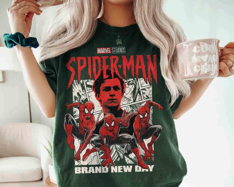 Puede incluir: Camiseta verde oscuro con un gr&aacute;fico de Spider-Man de Marvel Studios. El dise&ntilde;o incluye un retrato y tres figuras de Spider-Man en poses de acci&oacute;n, con el texto "SPIDER-MAN" y "BRAND NEW DAY".
