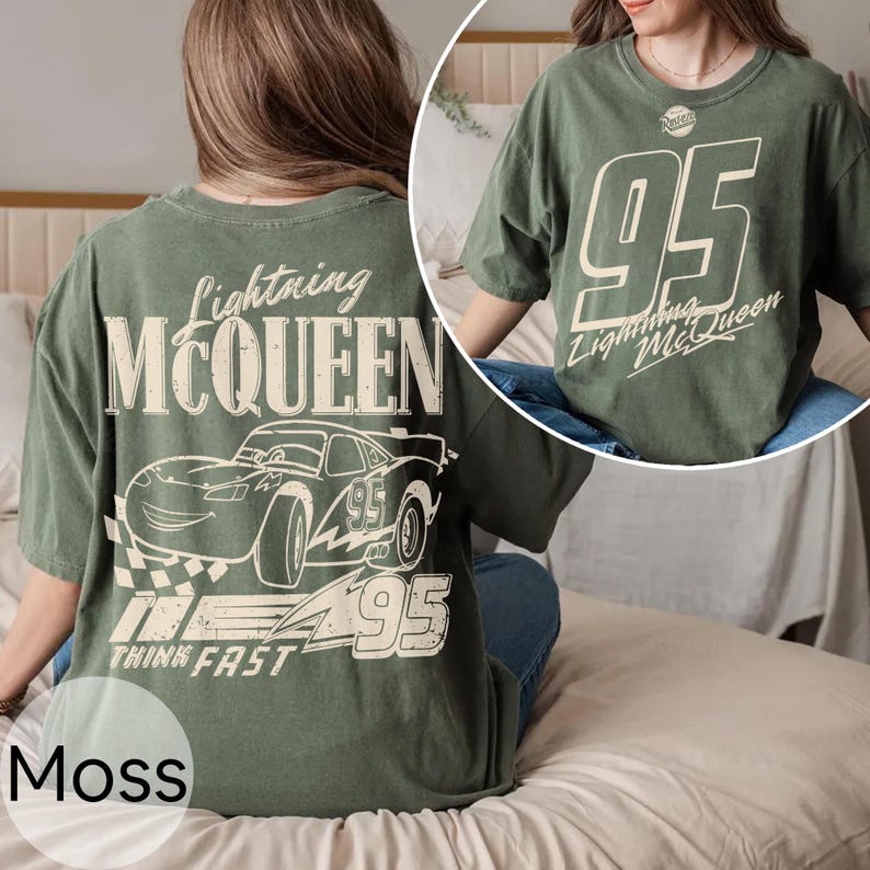 May include: Moss green t-shirt featuring Lightning McQueen graphics. The front displays "95" and "Lightning McQueen" text. The back showcases a race car illustration with "Lightning McQueen", "95", and "Think Fast" text. A comfortable, casual tee.