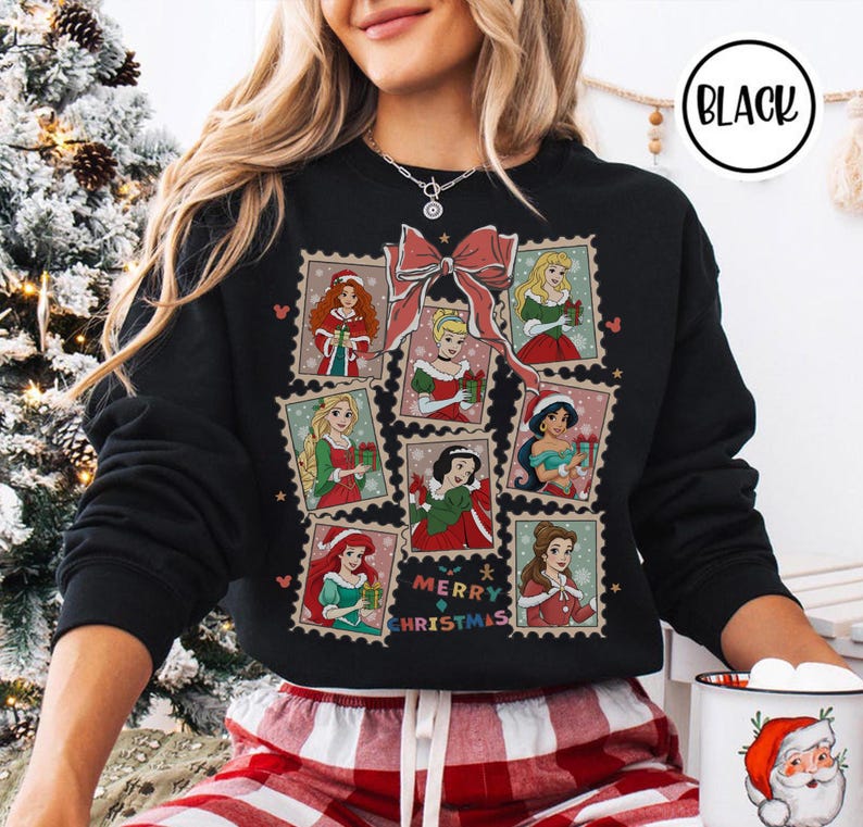 May include: Black sweatshirt featuring a festive design with princess illustrations in postage stamp frames. A large pink bow and the words "Merry Christmas" are also featured. The sweatshirt has a crew neck and long sleeves.