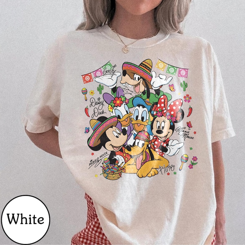 May include: Cream-coloured t-shirt with a vibrant graphic of Disney characters Mickey Mouse, Minnie Mouse, Donald Duck, Daisy Duck, Goofy, and Pluto, wearing sombreros. The design includes text and decorative elements.