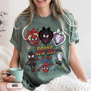 May include: Moss green t-shirt featuring a graphic of Spider-Man characters in heart-shaped designs, with the text "BRAND NEW DAY". The design includes various Spider-Man characters and a spider web background.