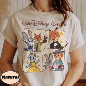 Peut inclure: T-shirt beige avec un motif color&eacute; des personnages de Zootopie, dont Judy Hopps et Nick Wilde. Le texte "Walt Disney World" est imprim&eacute; au-dessus du motif. Le t-shirt a des manches courtes et un col rond.