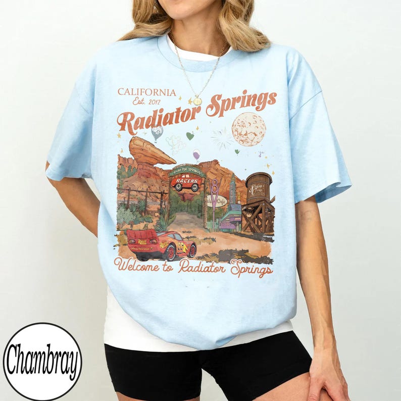 K&ouml;nnte beinhalten: Hellblaues T-Shirt mit einem Radiator Springs-Motiv, mit dem Text "CALIFORNIA Est. 2017 Radiator Springs" und "Welcome to Radiator Springs". Das Design zeigt ein rotes Rennauto und eine W&uuml;stenlandschaft.