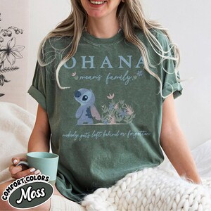 May include: Green t-shirt with the text "OHANA means family." and a cartoon illustration of a blue alien character. The shirt also features the phrase "nobody gets left behind or forgotten."