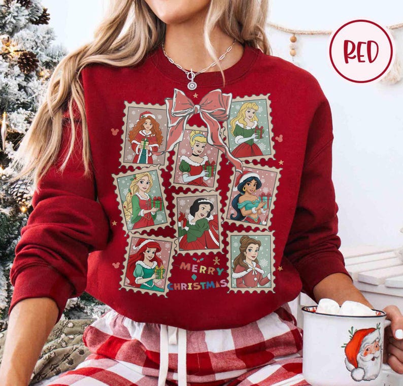 May include: A red sweatshirt featuring a collage of princess illustrations in postage stamp designs. A large pink bow is at the top, with the words "Merry Christmas" in the center. The sweatshirt is a solid red color.