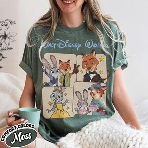 Peut inclure: T-shirt vert avec un motif repr&eacute;sentant des personnages du film Zootopie, dont Judy Hopps et Nick Wilde. Le t-shirt porte le texte "Walt Disney World" en haut et "Comfort Colors Moss" en bas.
