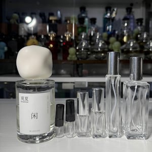 May include: A collection of clear glass perfume bottles and vials of various sizes. One bottle has a white label with Chinese characters and the words "in Summer" and "LEISURE". A white, cube-shaped object sits atop a bottle.