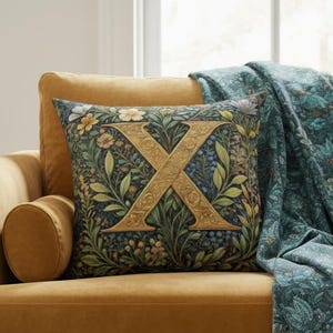 Op de afbeelding: Een mosterdgele fluwelen bank met een decoratief kussen met een gouden letter "X" op een bloemenachtergrond. Een turquoise sprei met een bloemenpatroon en franjes is over de bank gedrapeerd. Een bijzettafel met een vaas met droogbloemen staat links.