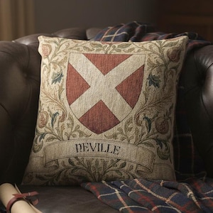 May include: A decorative pillow with a red and white cross design, the word "NEVILLE" is printed on a banner below the cross. The pillow is on a brown leather couch with a plaid blanket. Decorative items are on the couch.