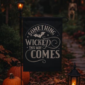 May include: A black Halloween garden flag with the text "SOMETHING WICKED THIS WAY COMES" in white script. The scene includes orange pumpkins, a lit lantern, and a pathway with a skeleton decoration in the background.