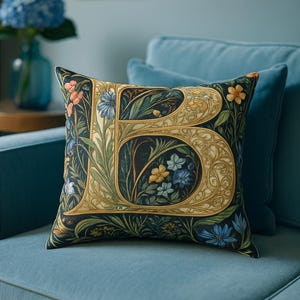 Könnte beinhalten: Dekoratives Zierkissen mit floralem Design und dem Buchstaben "B". Das Kissen hat einen dunklen Hintergrund mit bunten Blumen und Blättern sowie einen goldfarbenen Rand um den Buchstaben. Das Kissen liegt auf einem blauen Sofa.