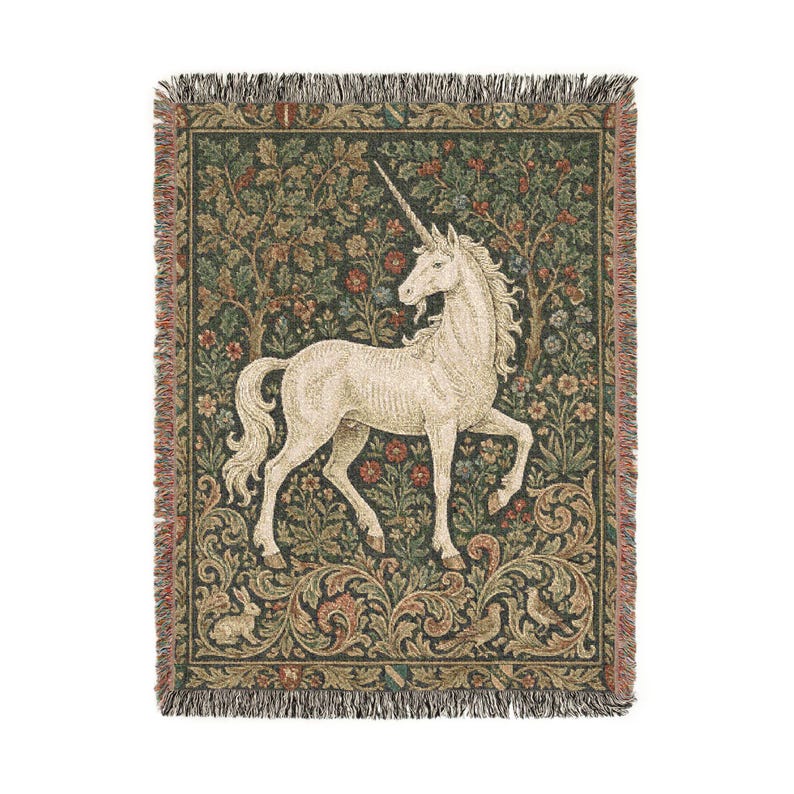 May include: A woven tapestry throw blanket featuring a white unicorn with a long horn, set against a backdrop of a forest with trees, flowers, and foliage in shades of green, red, and brown. The blanket has a fringed edge.