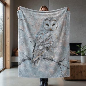 Könnte beinhalten: Hellgraue Decke mit detaillierter Illustration einer weißen Eule auf einem Ast. Die Eule hat große Augen und detaillierte Federn. Die Decke ist ein gemütliches Wohnaccessoire, das jedem Raum einen Hauch von Natur verleiht.