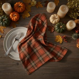 May include: A rustic table setting featuring a plaid orange and green napkin, white plates, and a silver fork. The table is decorated with mini pumpkins, candles, and autumn leaves. The wooden table provides a warm, inviting backdrop.