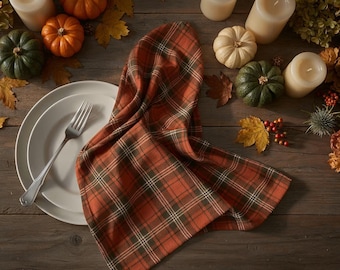 May include: A fall-themed table setting with a plaid orange and green napkin, white plates, and a silver fork. The table is decorated with mini pumpkins, candles, and fall foliage. The wooden table provides a rustic backdrop.