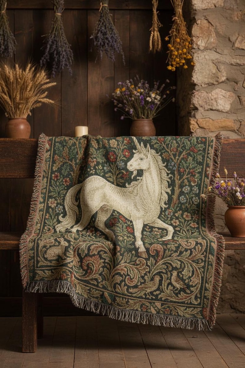 May include: A tapestry throw blanket featuring a white unicorn design on a dark green background with floral and tree patterns. The blanket has a fringed edge and is draped over a wooden bench. Decorative dried flowers and wheat are in the background.