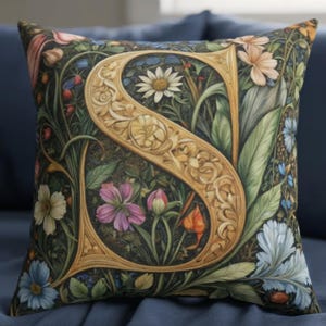 Könnte beinhalten: Dekoratives Zierkissen mit einem großen, verzierten goldenen Buchstaben "S", umgeben von einem detaillierten Blumendesign. Das Kissen hat einen dunklen Hintergrund mit bunten Blumen und Blättern in Rosa-, Blau- und Grüntönen.