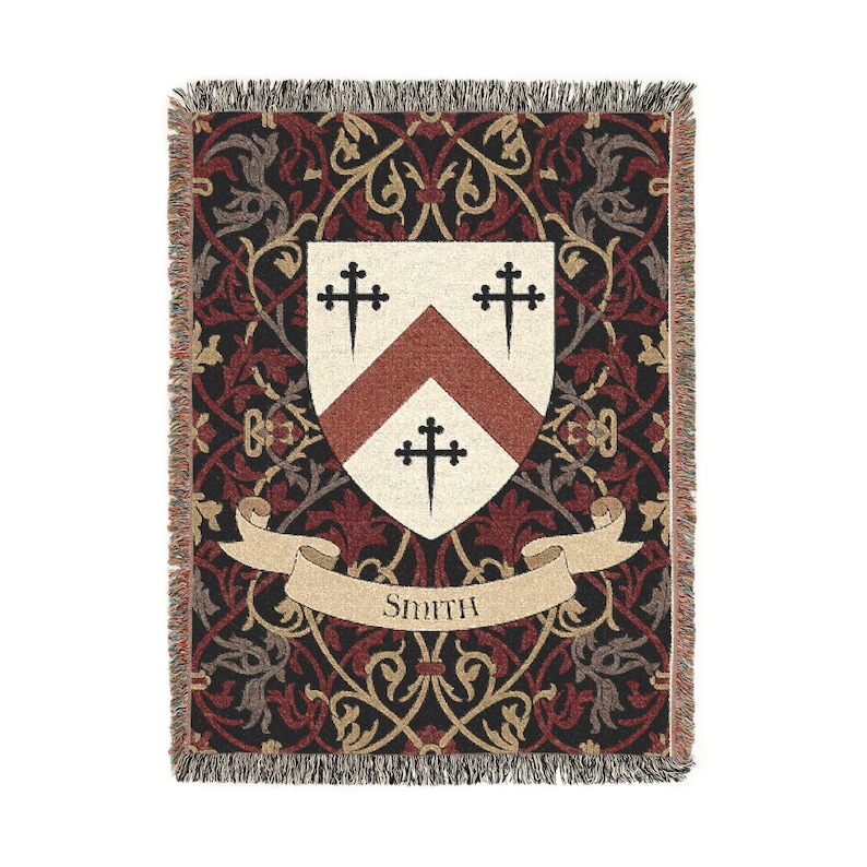 May include: Woven throw blanket with a heraldic crest design. The blanket features a cream-colored shield with a red chevron and three black crosses. The background is a dark red and black floral pattern, with the name "Smith" on a banner.