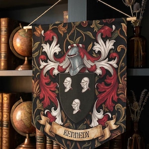 May include: A decorative banner featuring a family crest with the name "Kennedy" on a scroll. The crest includes a helmet, shields, and ornate red and white floral designs against a black background. The banner hangs in front of a bookshelf.