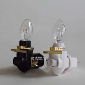 May include: Two night lights, one black and one white, with clear light bulbs. The lights have a switch and a plug.