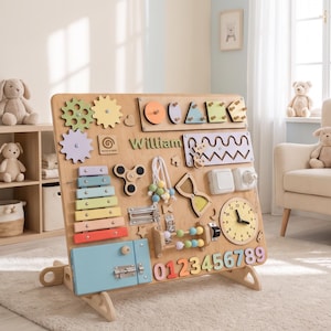May include: A wooden busy board for children featuring the name William, a colourful xylophone, gears, a clock, numbers zero through nine, a light switch, a latch, a spinner, and various tactile shapes in pastel and primary colours on a stand.