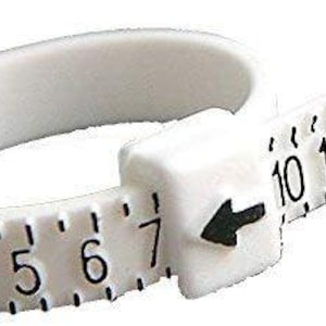 May include: A white plastic ring sizer with black numbers from 2 to 15. The ring sizer has a sliding mechanism with an arrow indicating the size. The numbers are printed in a clear, easy-to-read font.