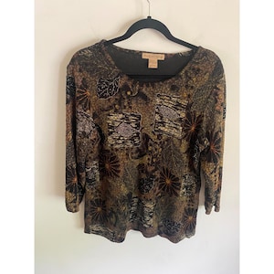 May include: A white ceramic mug with a black handle and the text "But First, Coffee" in a black, handwritten-style font. The mug is on a white surface.