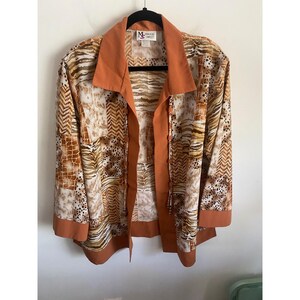 May include: A long-sleeve button-down shirt featuring a patchwork design of animal prints including leopard spots, zebra stripes, and giraffe patterns in shades of brown, tan, and white, with solid burnt orange trim on the collar, cuffs, and hem.